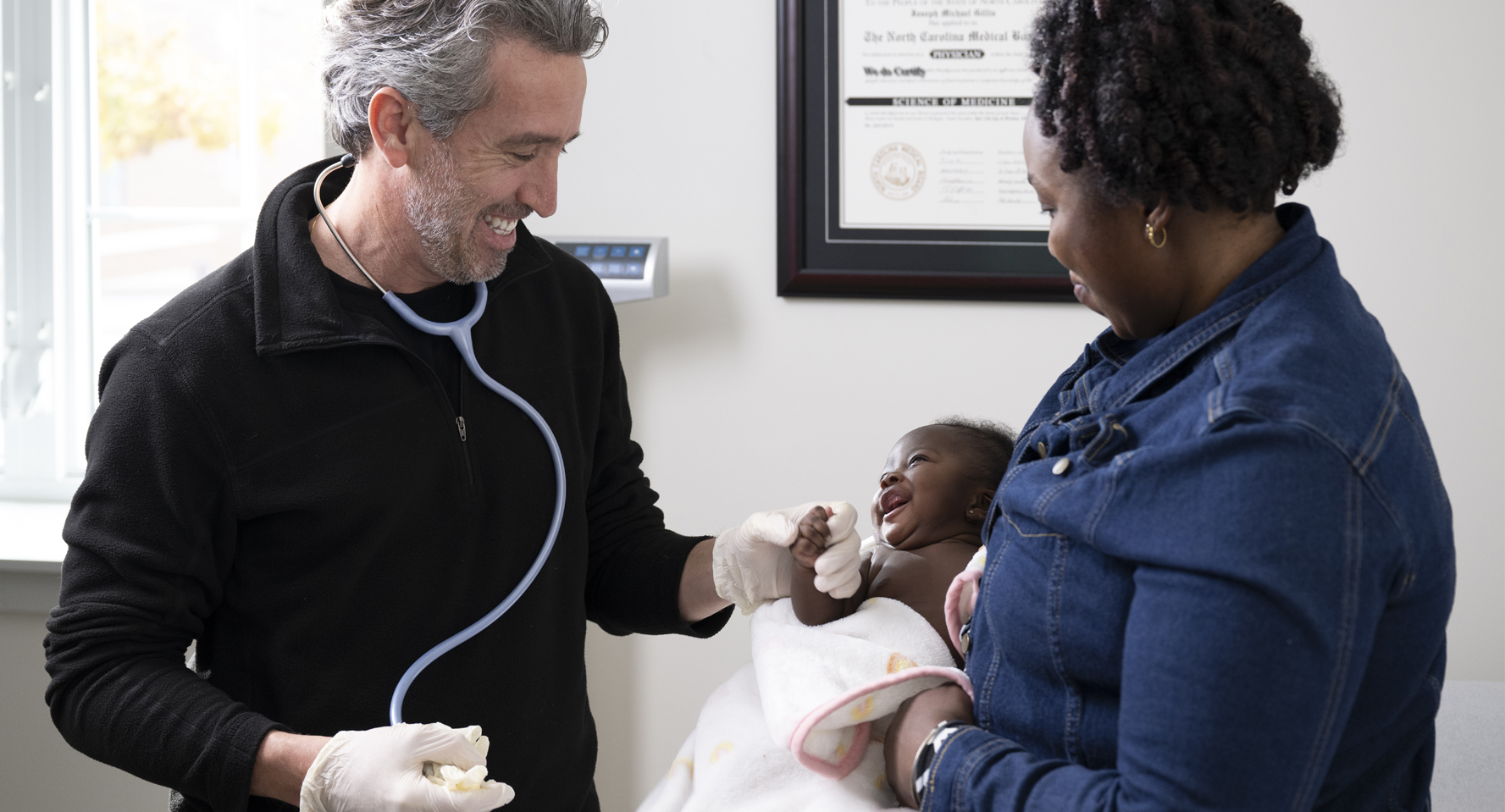 A photo of Dr. Joe Gillis in an examination room with a mom and baby